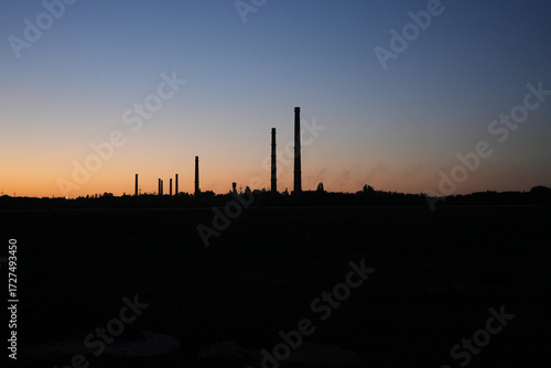 Silhouette of old factory chimneys at sunset with colorful sky gradient. Industrial landscape, environmental concept, dramatic skyline with tall pipes on the horizon.