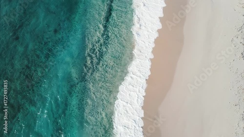 High-angle view of turquoise water meeting a light beige beach, with foamy waves