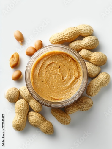 Peanut butter in glass jar with peanuts around it overhead studio shot on white background healthy food concept