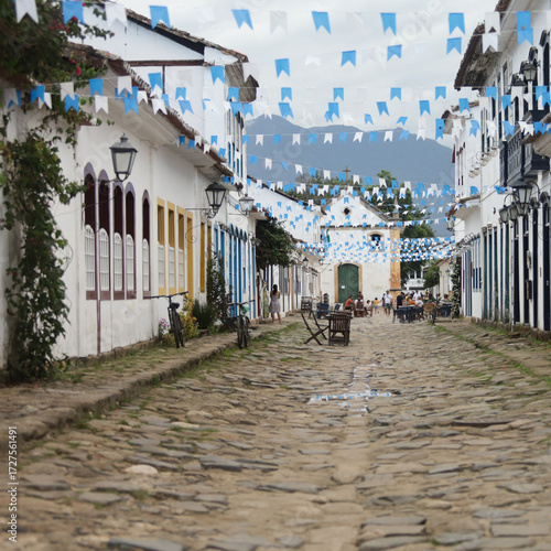 Rua de cidade histórica brasileira decorada com bandeirinhas azuis, destacando arquitetura colonial e atmosfera festiva.
