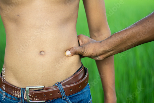 A hand pinching a persons stomach in a field
