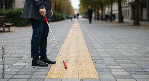 Blind person navigating tactile pathway with white cane on city street  