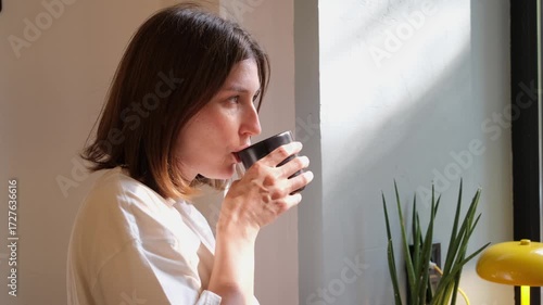 Caucasian Woman Drinking Coffee by Sunny Window