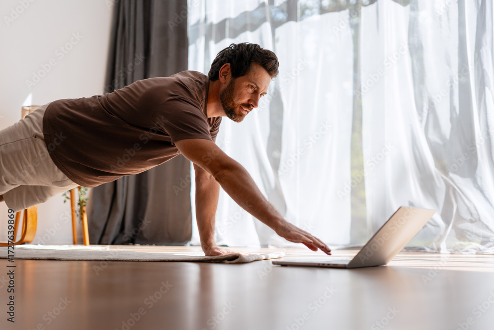 Fototapeta premium Handsome, middle aged man training at home with online fitness workout guidance