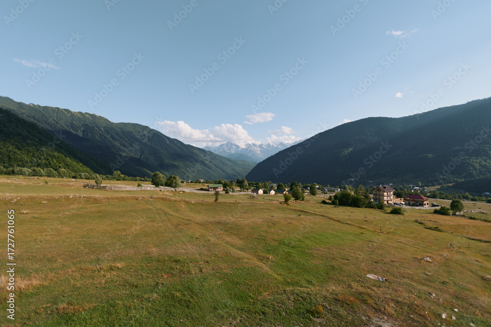 custom made wallpaper toronto digitalA tranquil countryside landscape unfolds across a wide valley framed by gentle hills. Sparse trees dot the fields beneath a clear blue sky, evoking peaceful, timeless natural beauty.