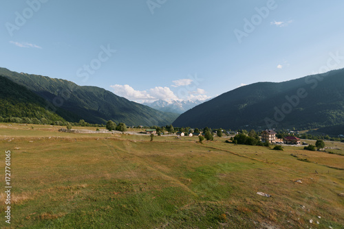 Wallpaper Mural A tranquil countryside landscape unfolds across a wide valley framed by gentle hills. Sparse trees dot the fields beneath a clear blue sky, evoking peaceful, timeless natural beauty. Torontodigital.ca
