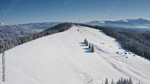 Stunning aerial view snow-covered mountain peak with a telecommunication tower, pine trees casting shadows on pristine slopes, and a breathtaking winter panorama. Winter wild nature travel background