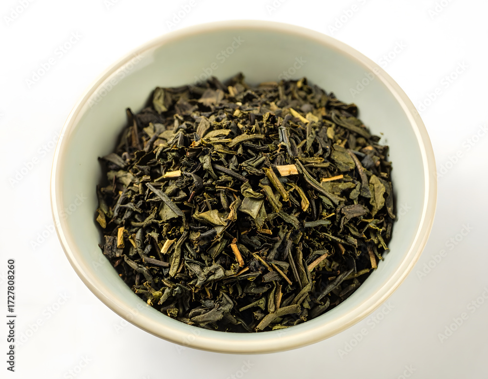 Fototapeta premium Loose leaf green tea leaves in a decorative bowl on a white background