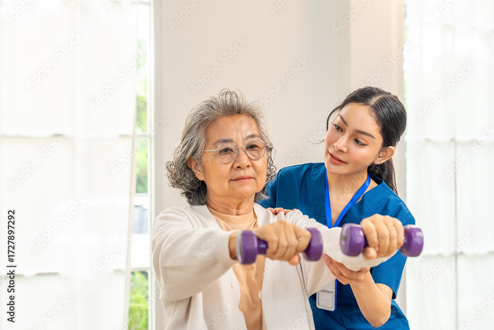 Fototapeta premium Asian woman physiotherapist caregiver teaching senior female patient exercise weight lifting dumbbell in bedroom. Elderly medical healthcare and wellness services, physical therapy and nursing home.