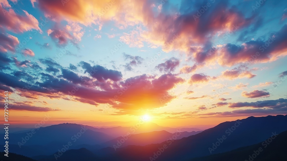 Fototapeta premium Vibrant sunset paints the sky with orange pink and blue hues over silhouetted mountain ranges