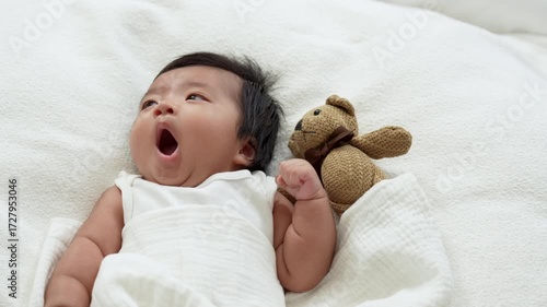 Asian Infant baby laying and yawn on white bed, ready to sleep.