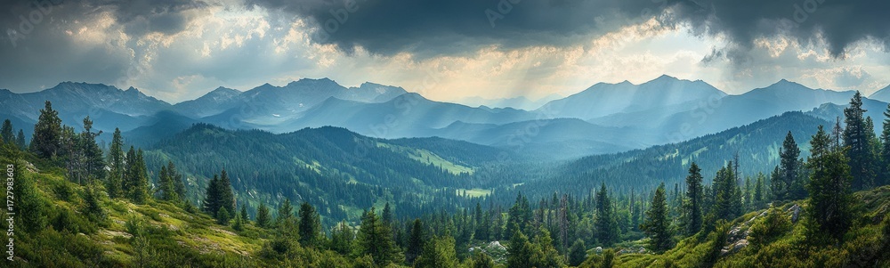 Obraz premium Vast mountain landscape with dense pine forest and rays of sunlight breaking through dramatic cloudy sky creating a serene and majestic atmosphere
