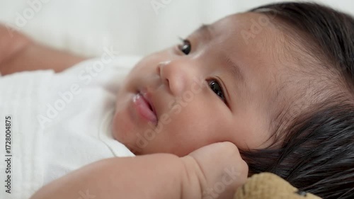 Asian newborn baby girls wearing a white bodysuit laying on the bed.