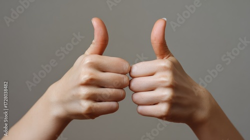Positive affirmation with two hands giving a thumbs up gesture symbolizing agreement, approval, and encouragement in a neutral background setting for creative use in various projects.