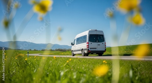 White passenger van driving on a road through a green field