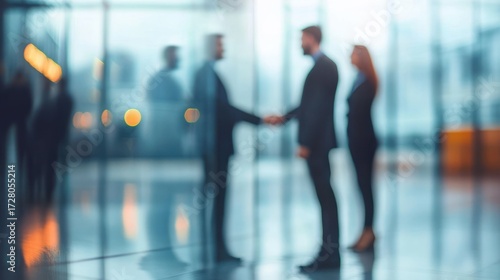 Two blurred businessmen shaking hands in a modern office environment with another woman standing nearby, conveying professionalism and agreement