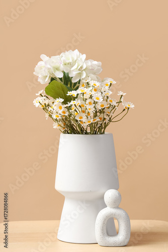 Foto Vase with artificial flowers on table against beige background
