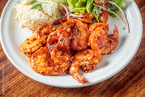 A plate of camarones a la diabla, spicy shrimp cooked in a rich red sauce, served with white rice and a side salad.