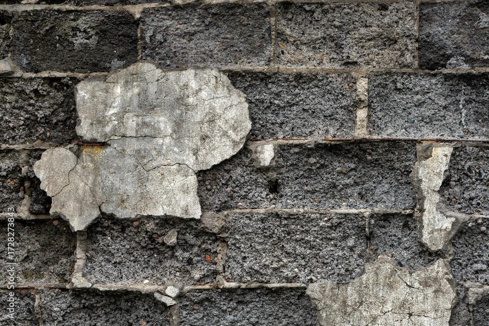 Fototapeta premium A textured view of a deteriorating stone wall with cracked, peeling plaster, showing layers of wear and age, highlighting urban decay and rustic architectural details