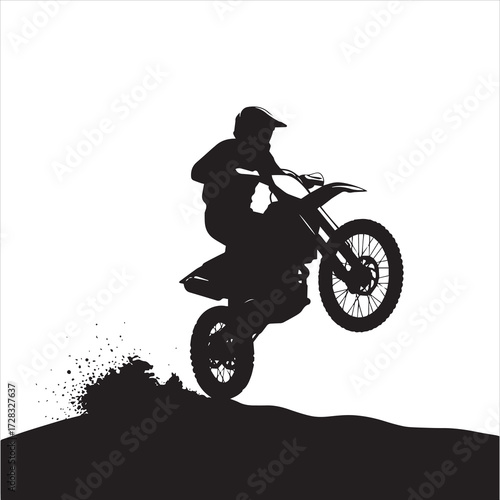 Silhouette of a motocross rider performing a wheelie jump on a dirt bike over a small hill, with dirt spraying from the rear tire.