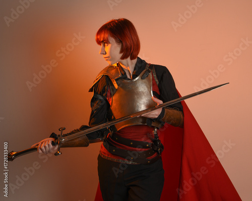 portrait of Fantasy warrior woman model, holding sword weapon, historical medieval armour costume with red fairytale cloak, strong fantasy knight. isolated studio background golden cinematic lighting.