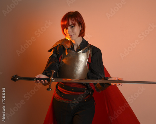 portrait of Fantasy warrior woman model, holding sword weapon, historical medieval armour costume with red fairytale cloak, strong fantasy knight. isolated studio background golden cinematic lighting.