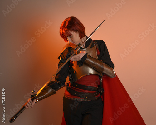 portrait of Fantasy warrior woman model, holding sword weapon, historical medieval armour costume with red fairytale cloak, strong fantasy knight. isolated studio background golden cinematic lighting.