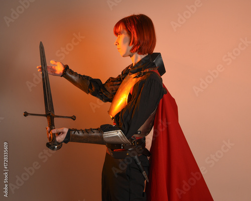 portrait of Fantasy warrior woman model, holding sword weapon, historical medieval armour costume with red fairytale cloak, strong fantasy knight. isolated studio background golden cinematic lighting.