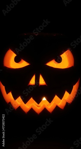 A carved pumpkin with an angry face glows in the dark, illuminated from within, creating a spooky Halloween atmosphere.