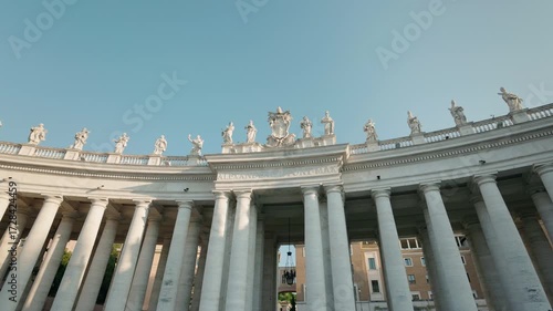 Colonnade of St. Peter's Square with statues of saints and clear blue sky in Vatican City, Rome, Italy