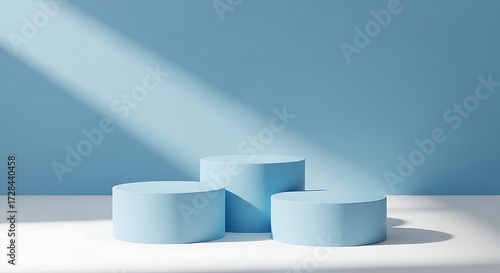 Three light blue cylindrical podiums of varying heights arranged on a white surface with soft light