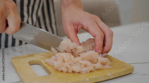Mother cooking dinner for children, cutting chicken fillet, fresh organic food. Closeup view of female hands with knife and chopping board on home kitchen table, nutrition for health and slenderness