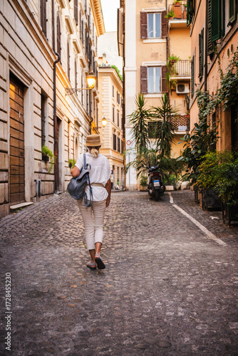 Photography Woman with backpack and straw hat walking along a narrow cobblestone street in R