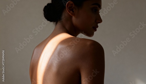 A womans back is illuminated by a dramatic shaft of light, highlighting her skin texture