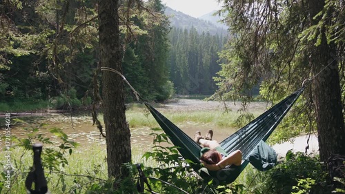 A woman hiker is resting in a hammock overlooking a mountain lake