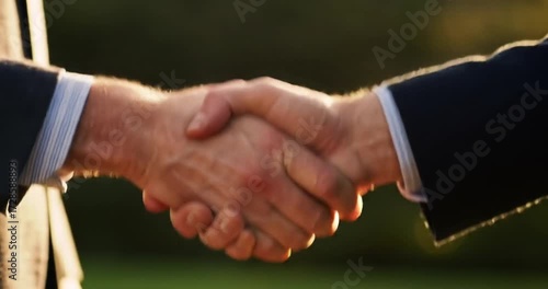 Two business professionals shaking hands outdoors at sunset
