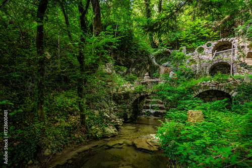 A small arched waterfall with a pool, by the old abandoned mill ruins in the forest near the Stomaž village near Ajdovščina, Slovenia