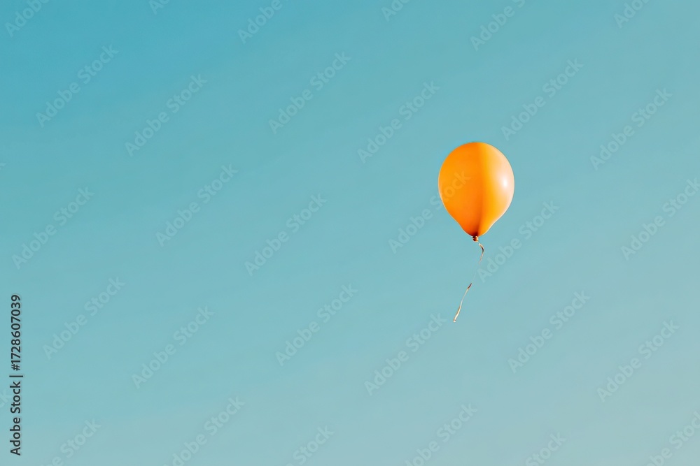 Obraz premium Orange balloon floats freely in air against clear blue background, creating a minimalist, simple atmosphere with clean lines and unattached, carefree aesthetic.