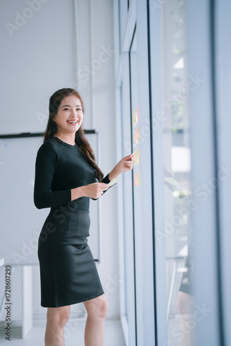 Free Download Asian businesswoman working in a bright modern office. Actively planning strategy and organizing tasks using colorful sticky notes on a glass window. Demonstrating business efficiency and bright ideas - GFXLoad