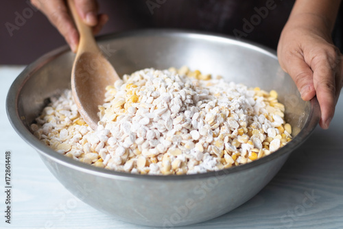 hands holding a bowl, A hand hold wooden scoop mix cooked soy beans and white powder of tempeh starter ( Rhizopus oligosporus or Rhizopus oryzae) in stainless steel bowl on white table