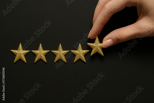 Hand Placing Fifth Golden Star on Dark Surface for Excellent Rating.