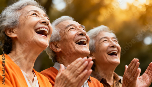 Happy senior friends laughing together outdoors. Cheerful group of elderly Asian people enjoying a fun moment in a park. Healthy active lifestyle in retirement. Togetherness.