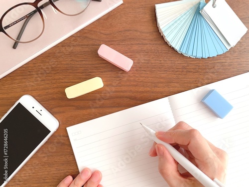 A woman's hands writing in a notebook at a wooden desk