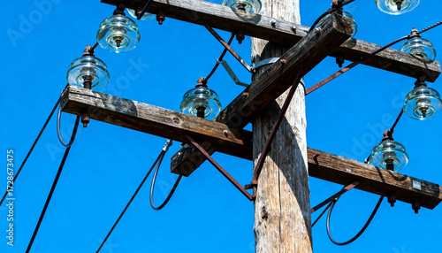 Old rustic wooden electricity pole with glass insulators and power lines. Concept for energy supply, electrical grid, communication, connection, and infrastructure technology.