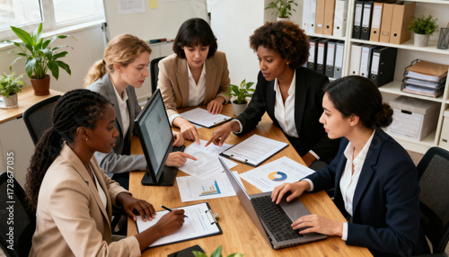 A multiethnic group of female professionals in a strategic meeting. Businesswomen collaborating, analyzing financial data, charts on laptops and paper for corporate planning.