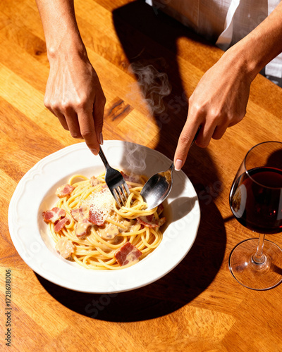 Steam rises as the pasta is twirled with fork and spoon—creamy sauce, crispy bacon, and grated cheese on a warm wooden table