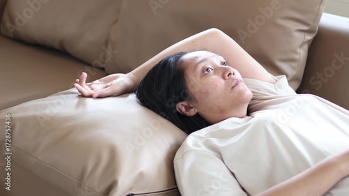 Asian woman lying on the sofa with a sad, depressed and unhappy face. She might be experiencing depression.