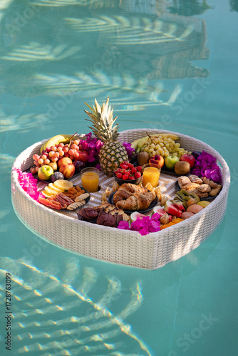 Luxury floating breakfast tray with tropical fruits, pastries, and juice in swimming pool