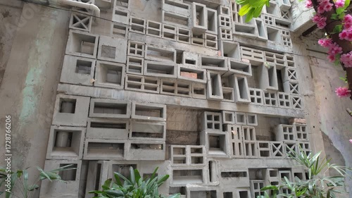 An innovative architectural wall design featuring a geometric concrete block pattern complemented by lush green foliage, creating a harmony between urban aesthetics and nature.