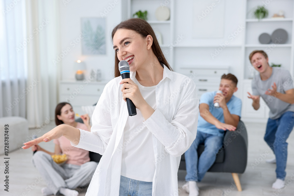 Obraz premium Young woman singing karaoke with friends at home, selective focus
